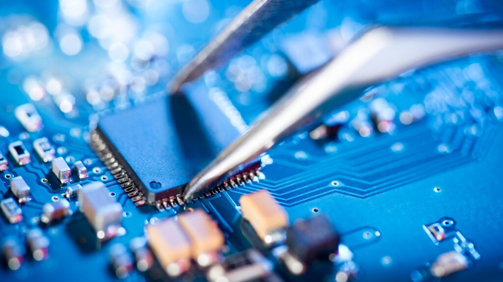 Tweezers grab a microchip on a printed circuit board
